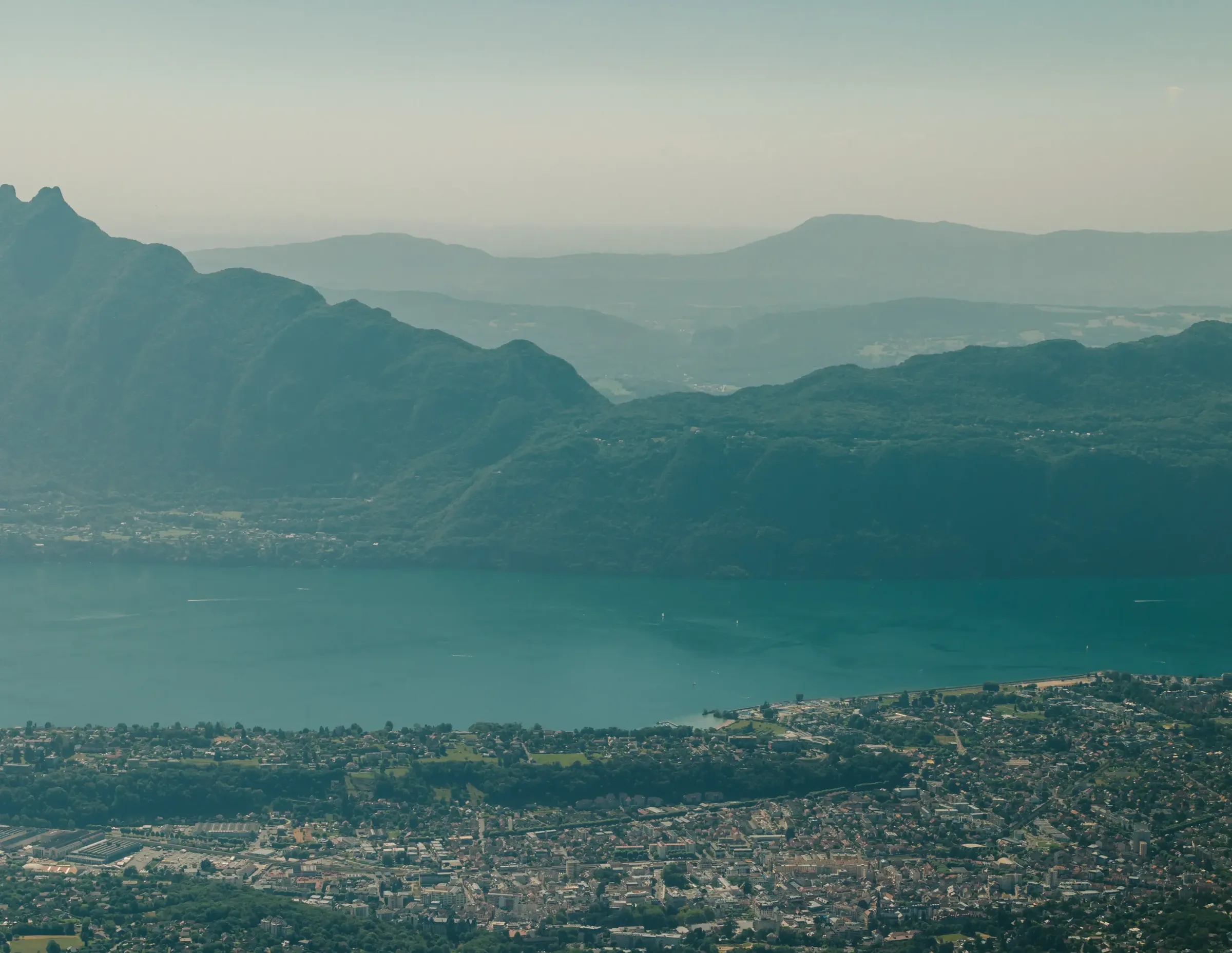 City bordered by a lake surrounded by mountains with varied relief and dense vegetation