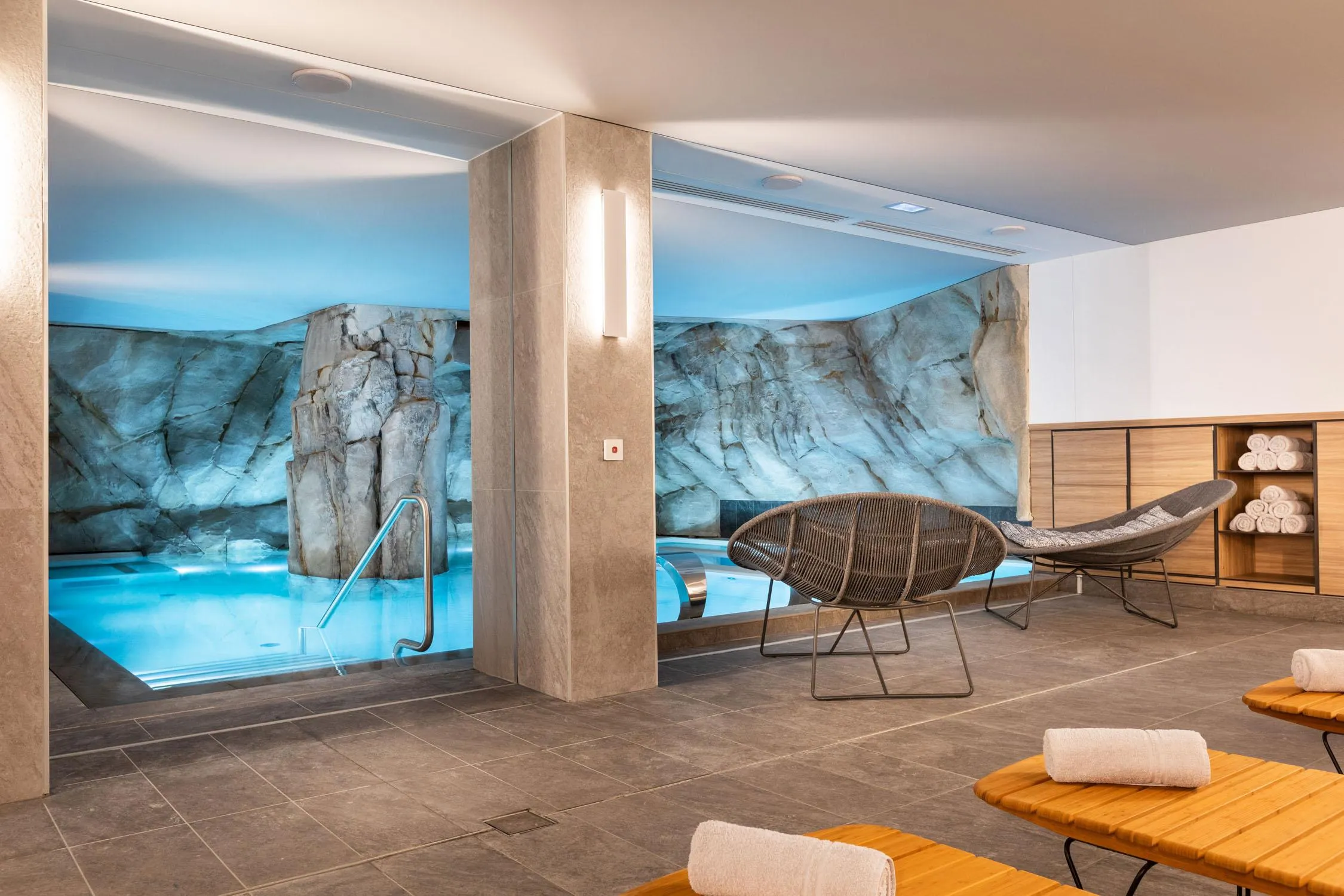 Relaxation room with sun loungers, towels, and a view of a pool with painted rocks on the wall
