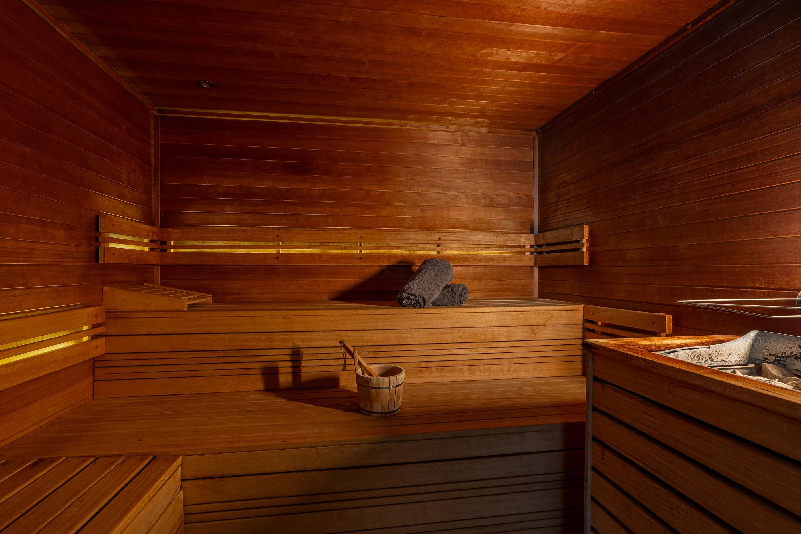 Interior of a wooden sauna with benches, a wooden bucket and ladle, and hot stones