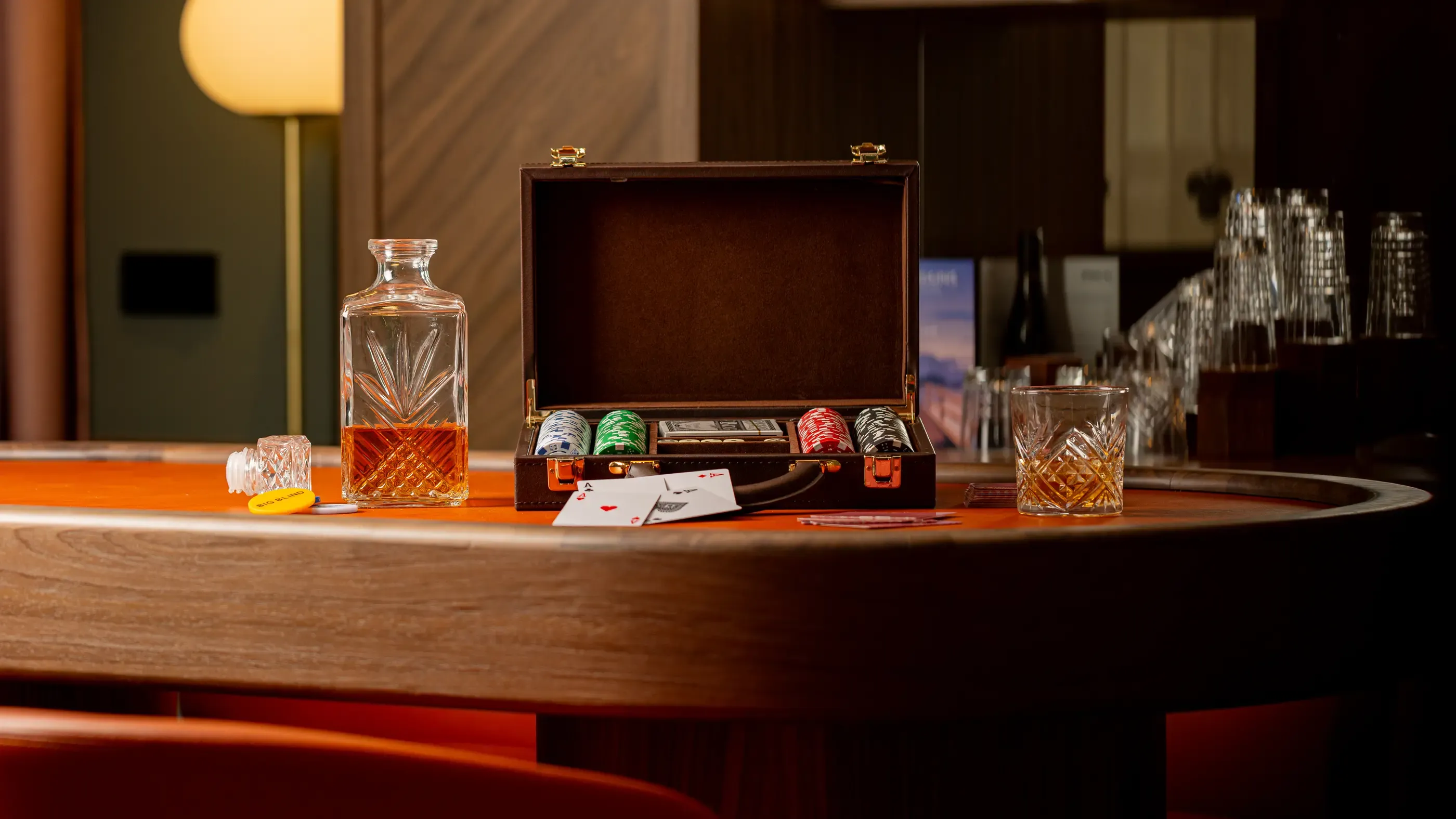 A table with an open poker case, chips, cards, a glass, and a bottle of whisky.