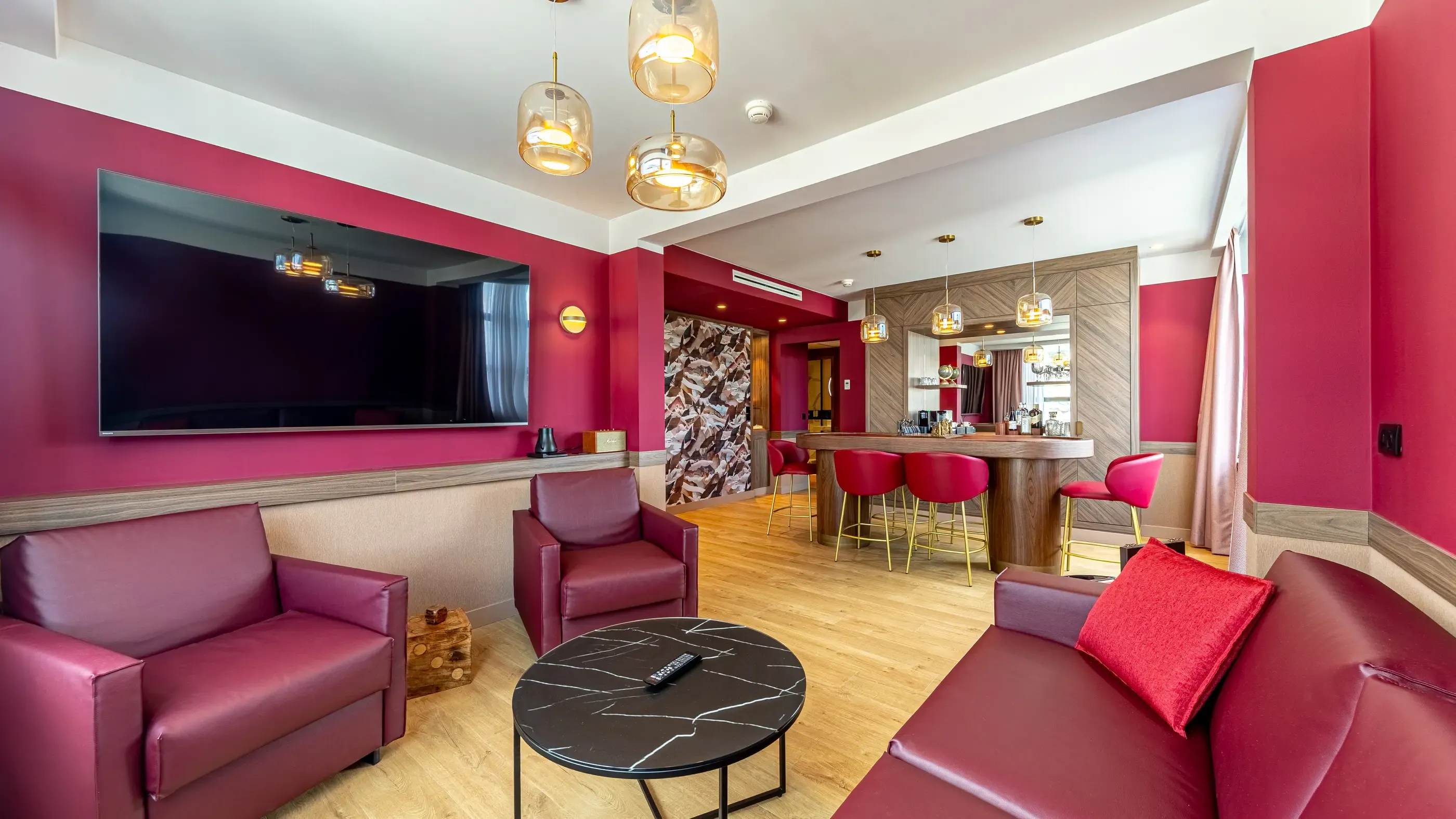 Living room with red sofas and armchairs, black marble coffee table, bar with stools and wall-mounted screen