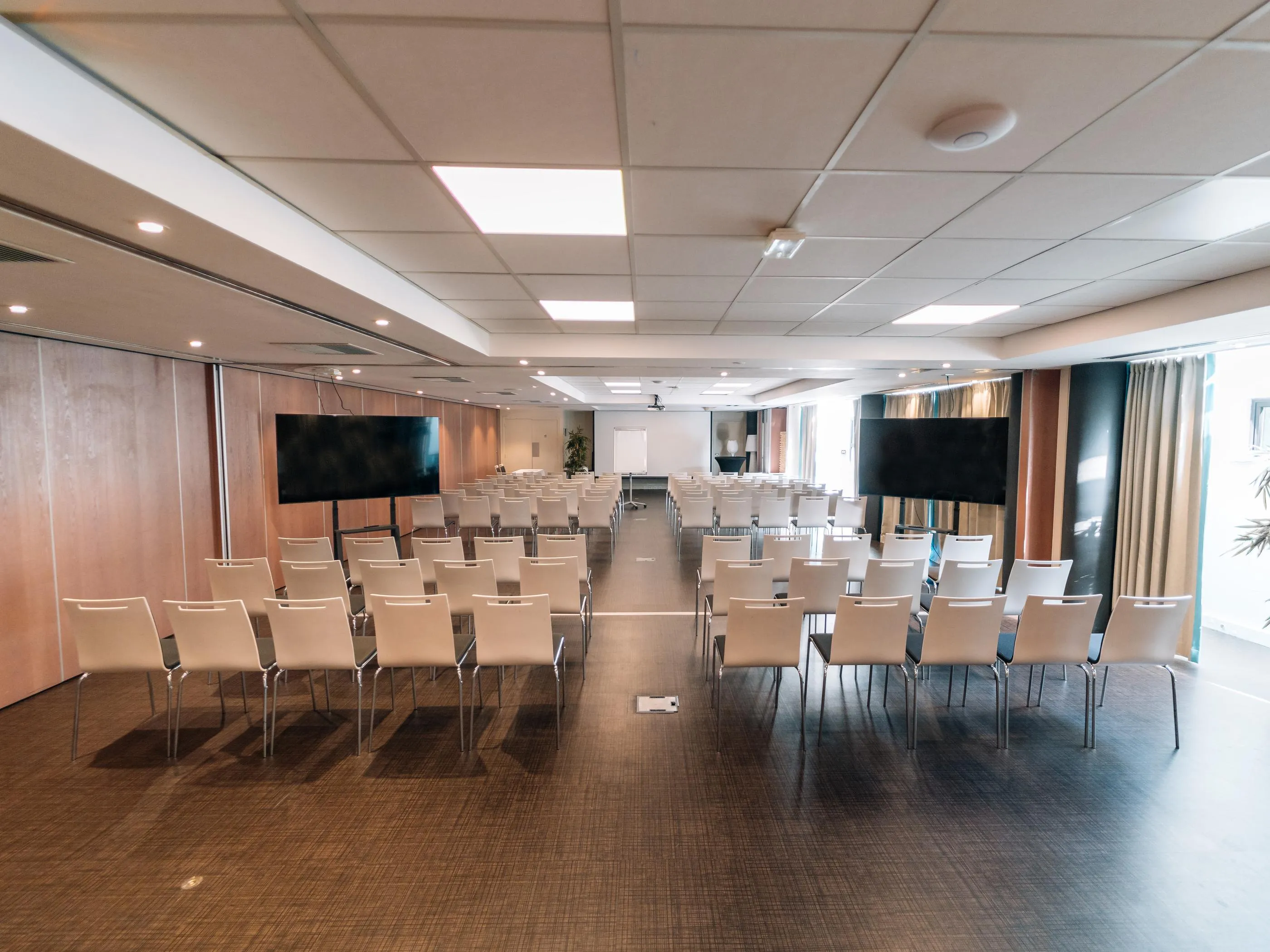Leerer Konferenzraum mit Sitzreihen, zwei Bildschirmen und Deckenbeleuchtung