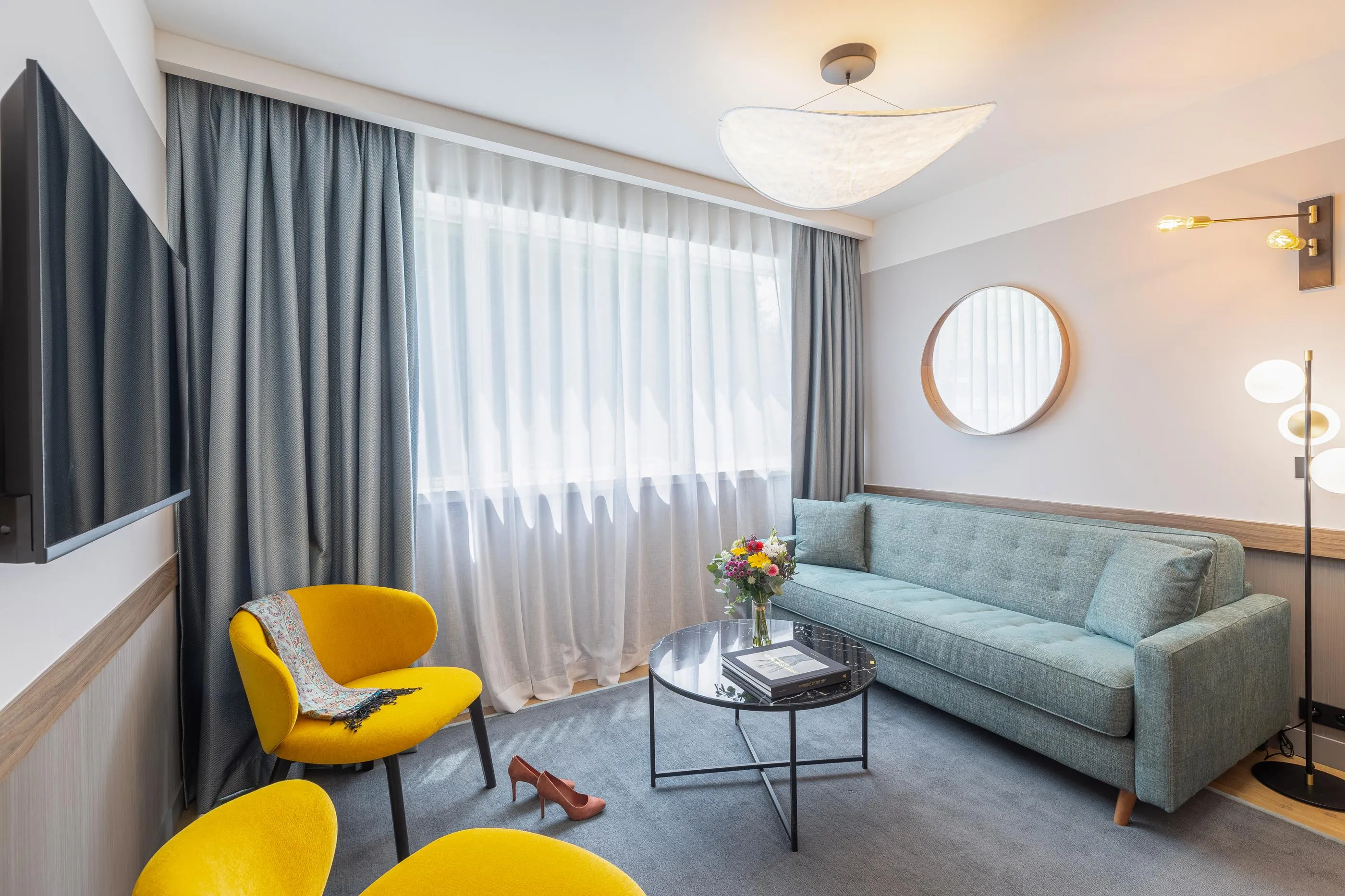 Living room with green sofa, two yellow armchairs, coffee table, flowers and wall-mounted television