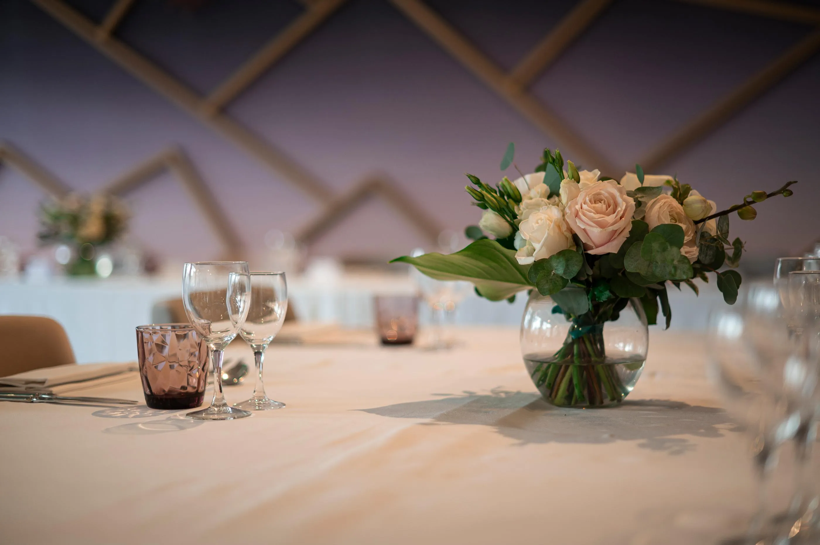 Tisch gedeckt mit Gläsern, einer getönten Glaskaraffe und einer Vase mit hellen Rosen und Blättern