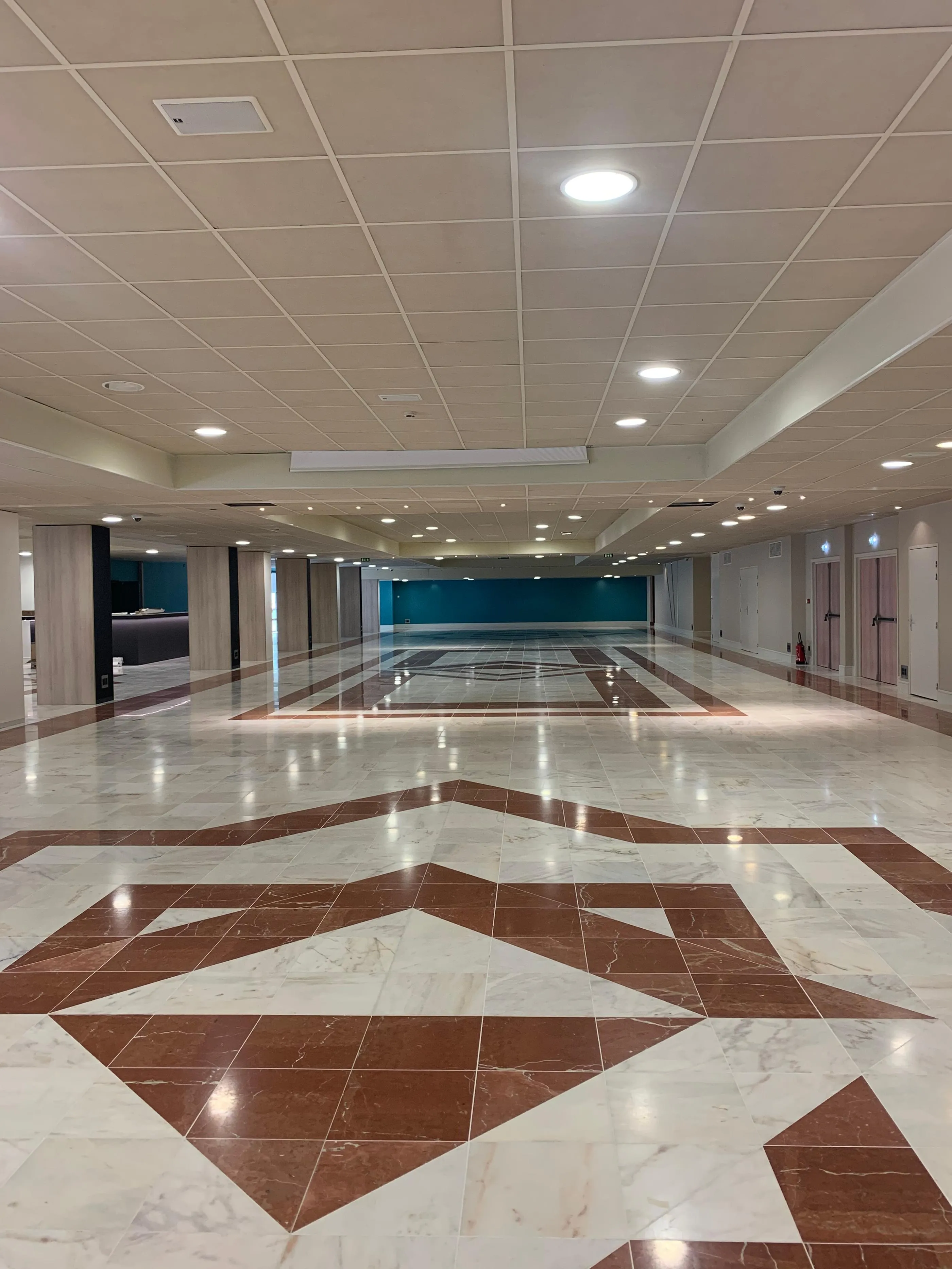 Große Innenhalle mit marmoriertem Boden in geometrischen Mustern und beleuchteter Deckenverkleidung